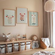 Three framed nursery prints featuring cute soft-colored farm animals above a wooden storage unit with fabric bins in a cozy, neutral-toned children's room.