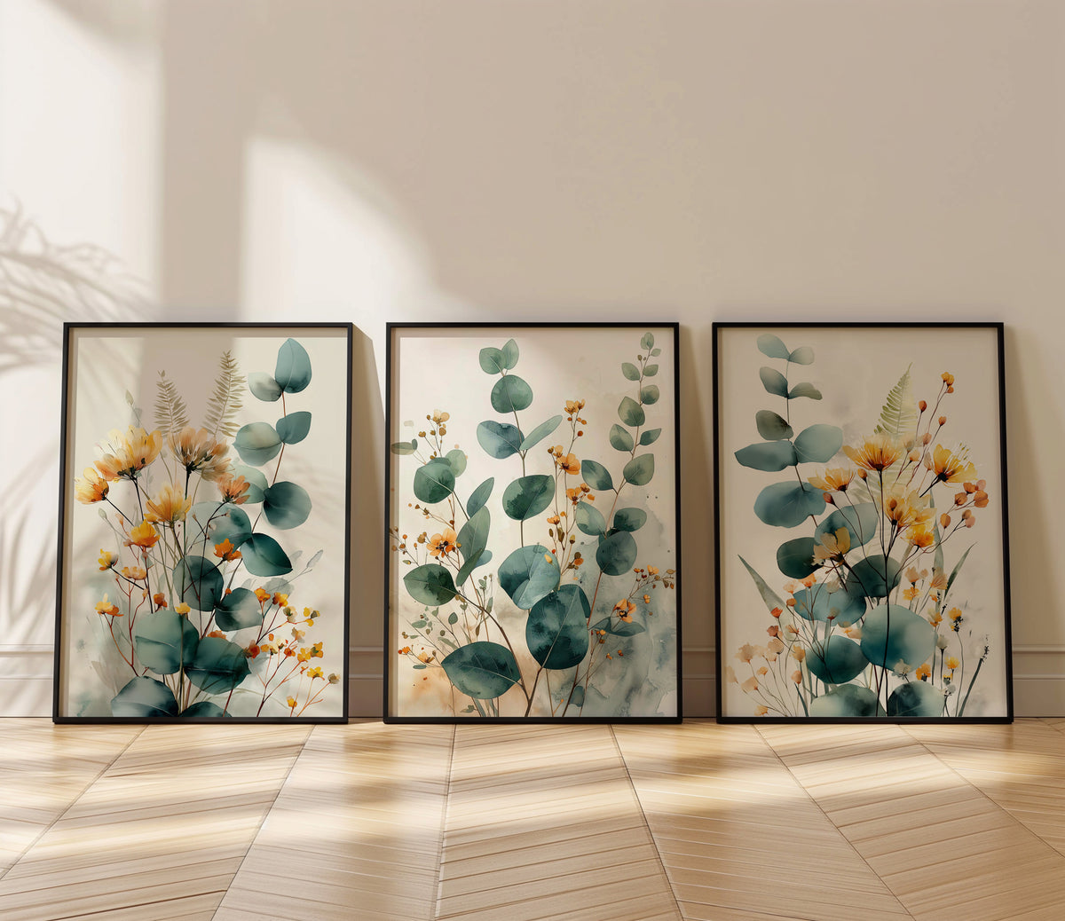 Three framed botanical art prints with eucalyptus leaves and yellow-orange wildflowers, leaning against a beige wall on a light wood floor.