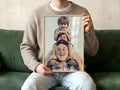 Person sitting on a green sofa holding a framed custom print photo of three generations of men smiling with a neutral background and natural light.