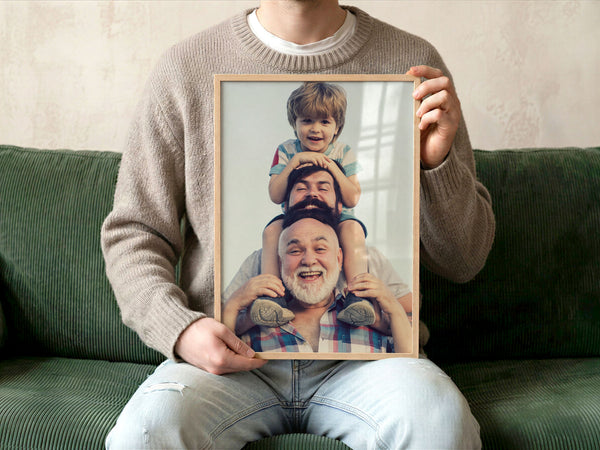 Person sitting on a green sofa holding a framed custom print photo of three generations of men smiling with a neutral background and natural light.