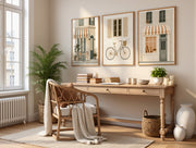 A styled interior room with a wooden desk, wicker chair, plants, books, and three framed street-art prints hanging on the wall above the desk.