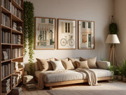 A cozy living room scene with a wooden daybed styled with beige and cream pillows and a throw blanket. Above the daybed are three framed art prints depicting storefronts and a bicycle.
